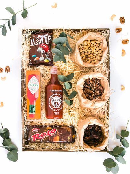 Gift box with M&M's, Rolo, Tabasco, Sriracha sauce, nuts, and biltong surrounded by decorative foliage.