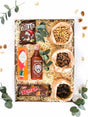 Gift box with M&M's, Rolo, Tabasco, Sriracha sauce, nuts, and biltong surrounded by decorative foliage.