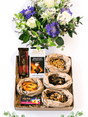 Indulgent snack box with luxury nuts, chocolates, nougat, and a fresh floral arrangement in a vase, perfect for gifting.